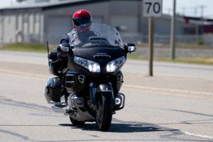 A motorcyclist rides a large touring bike on a road with a speed limit sign visible.