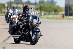 A motorcyclist leads a group of riders down a road with buildings visible in the distance.