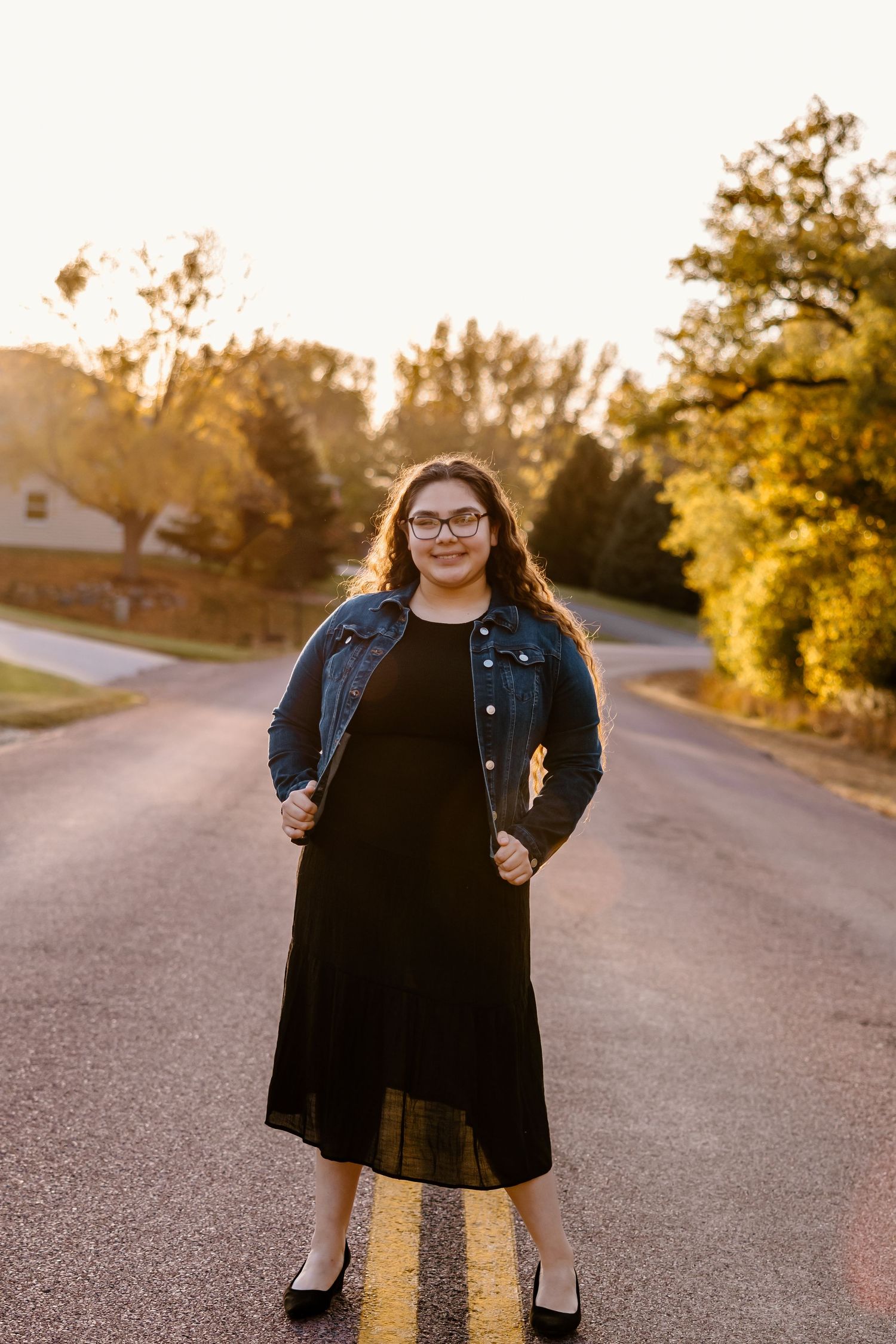 Person in denim jacket poses on asphalt road during golden hour sunset.