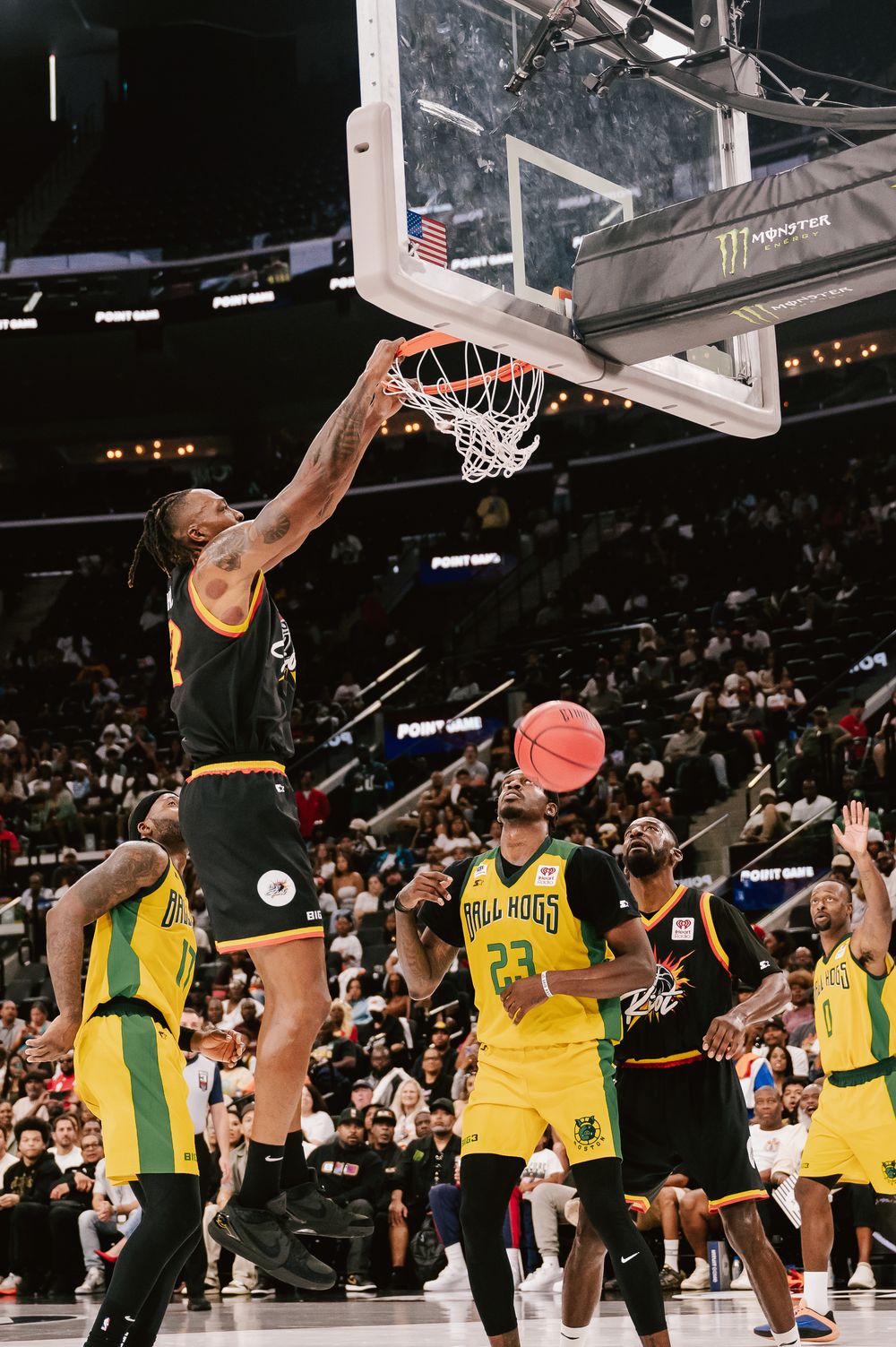 Basketball player in yellow and black uniform performs a powerful slam dunk during a professional game.