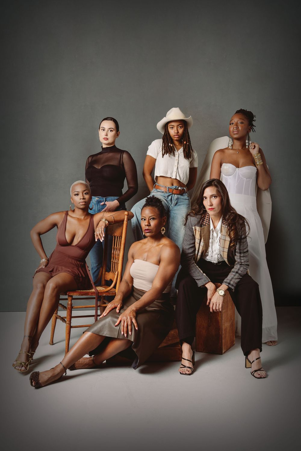 A stylish group portrait series showing diverse models in casual attire posing together on wooden chairs against a gray backdrop.