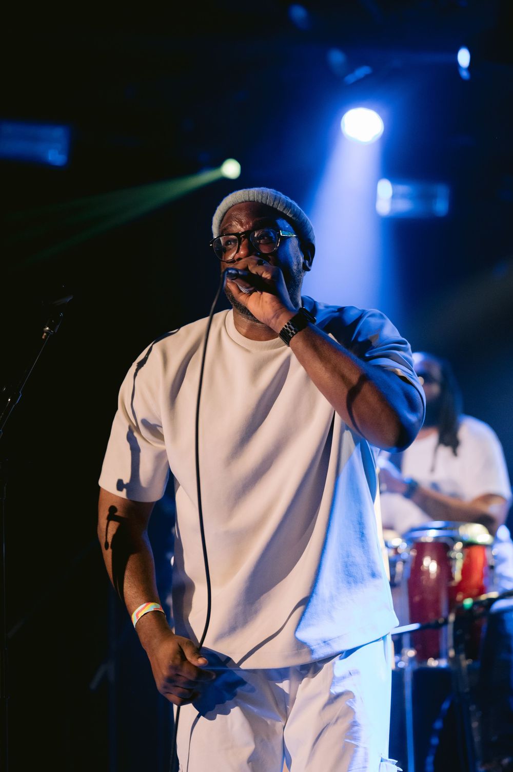 Performer in white t-shirt singing passionately on stage with dramatic blue lighting and microphone during live show.