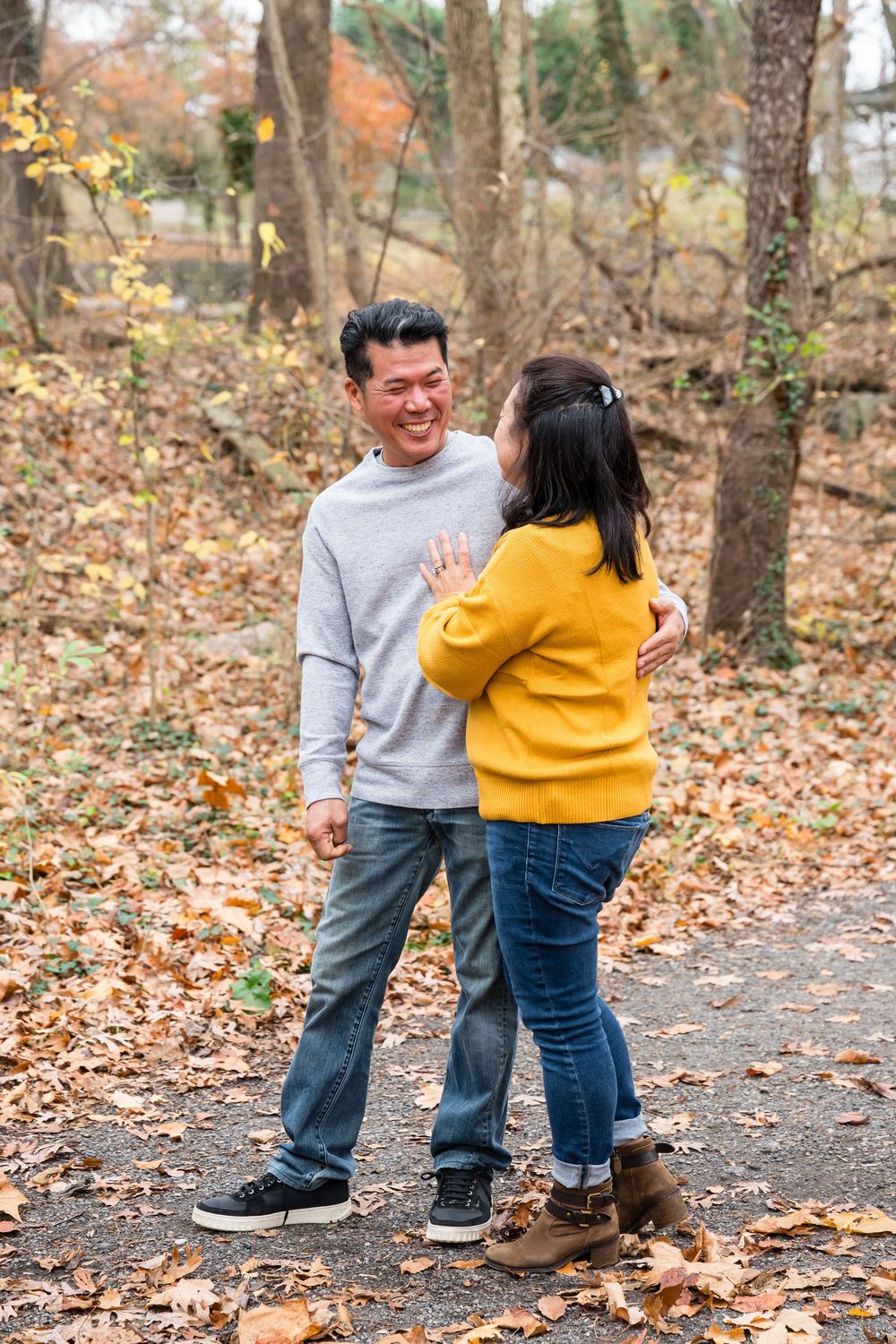 A couple shares a tender moment together on a path covered in fallen autumn leaves.