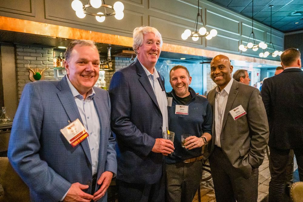 A group of professionals enjoying drinks and conversation at a networking event under chandelier lighting.