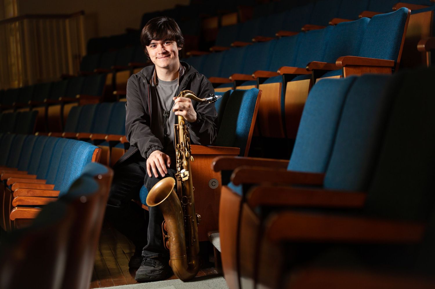 A saxophone player sits for a portrait in an empty audience.