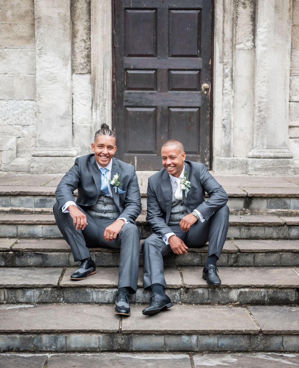 Two people in matching suits share a relaxed moment sitting on stone steps.