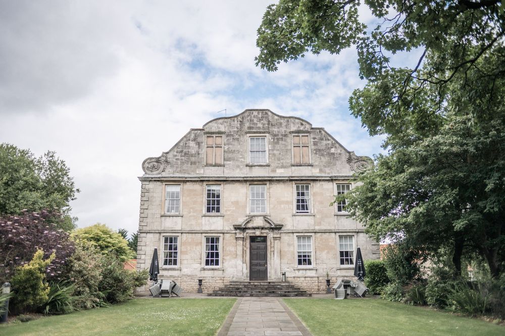 Stately Georgian manor house with symmetrical windows and grand entrance surrounded by gardens.