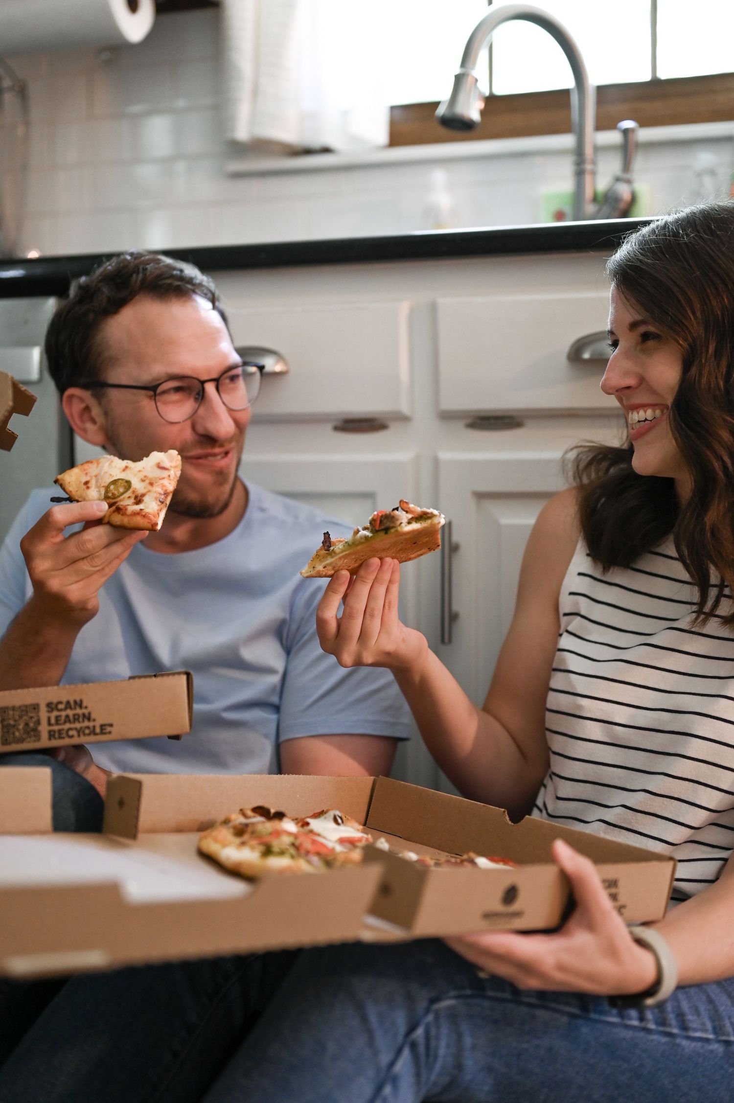 A couple shares pizza and laughs in their modern kitchen.