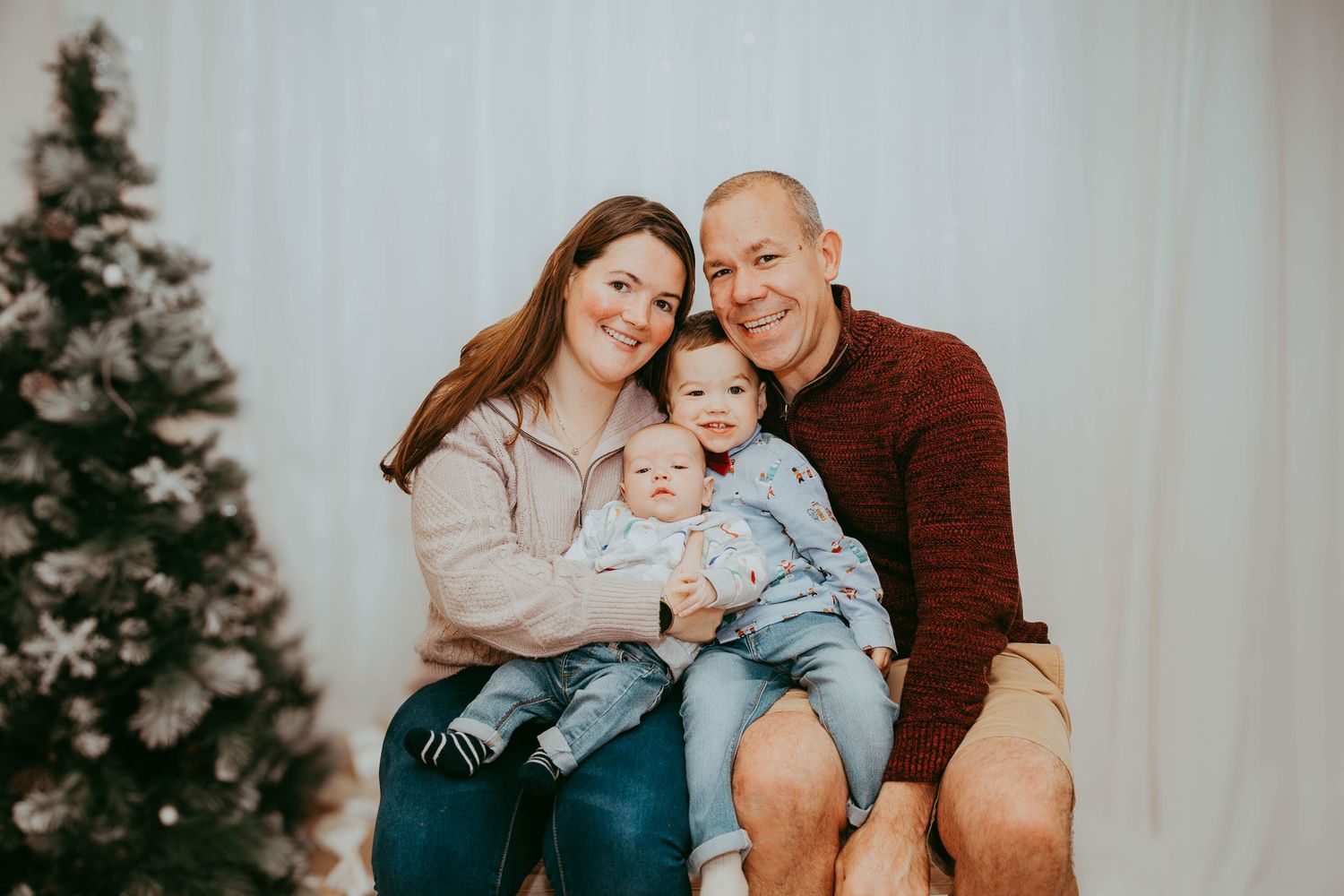 Casual winter family portrait in cozy sweaters beside Christmas tree.