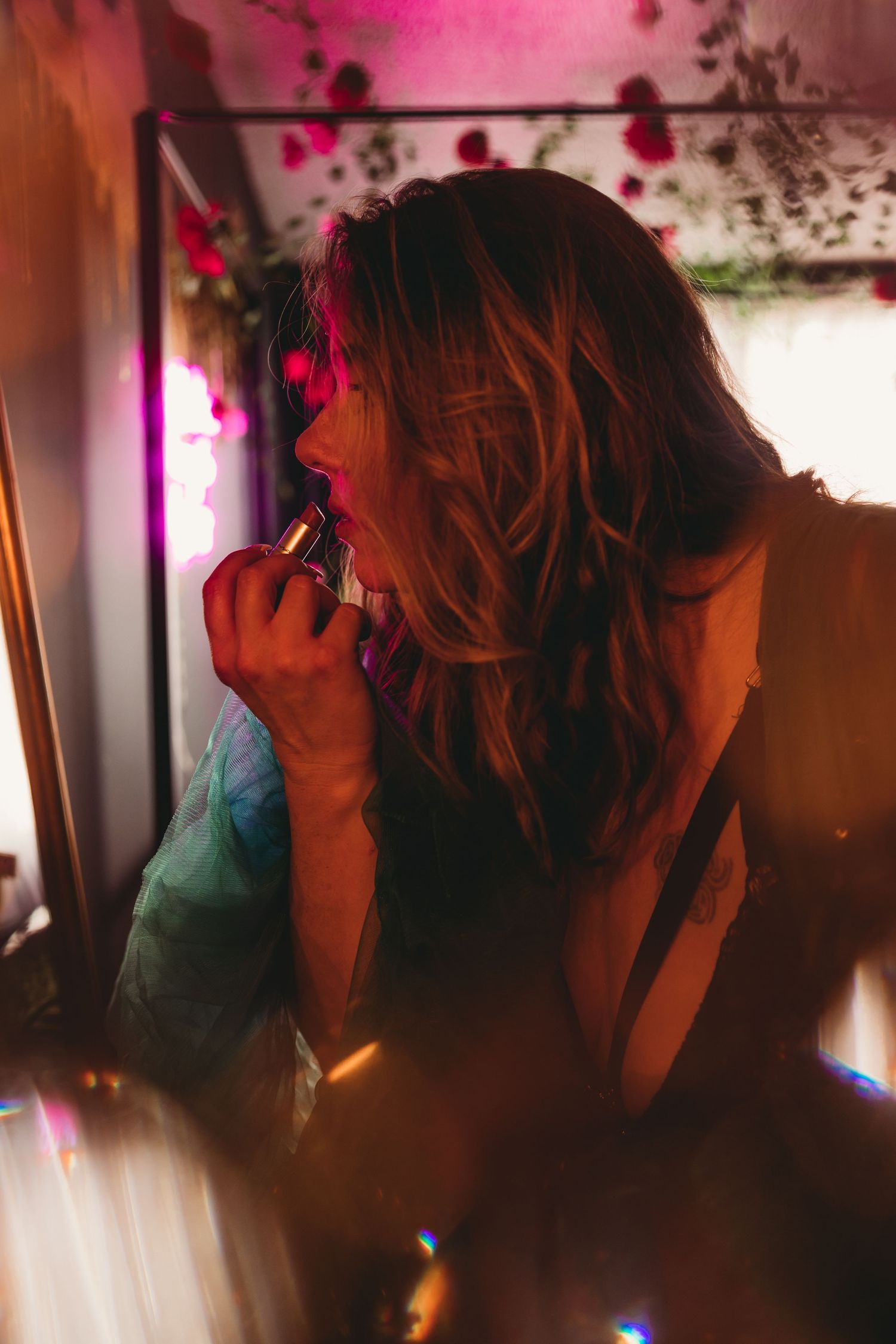 Silhouetted figure applying lipstick in moody lighting with pink and purple hues and sparkling light effects.