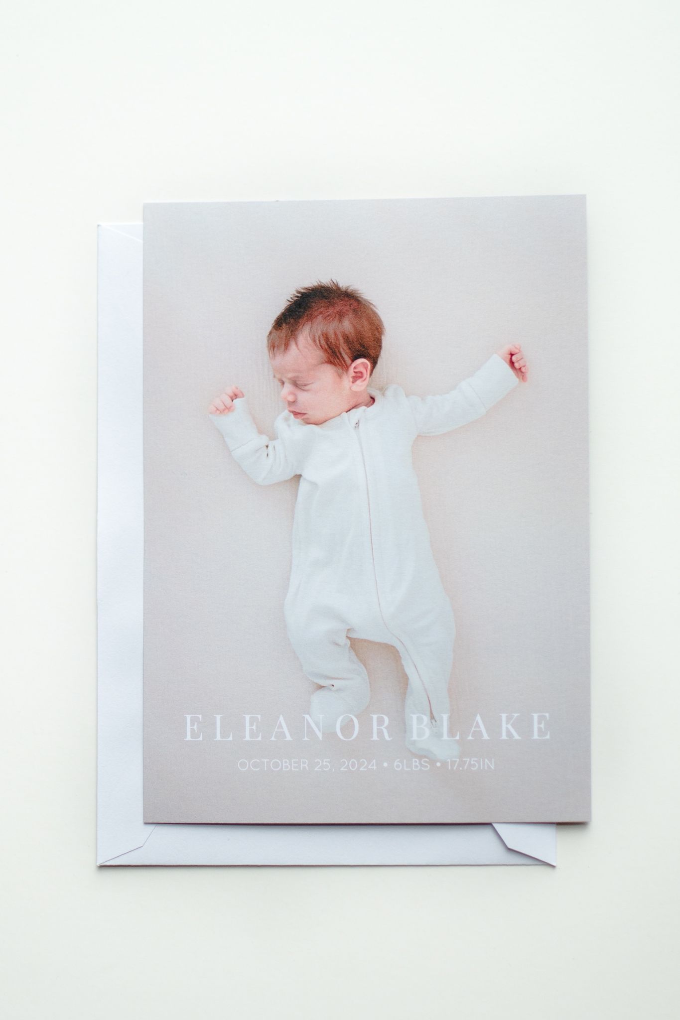 Birth announcement card featuring a sleeping baby in a light blue onesie lying on a neutral gray background.