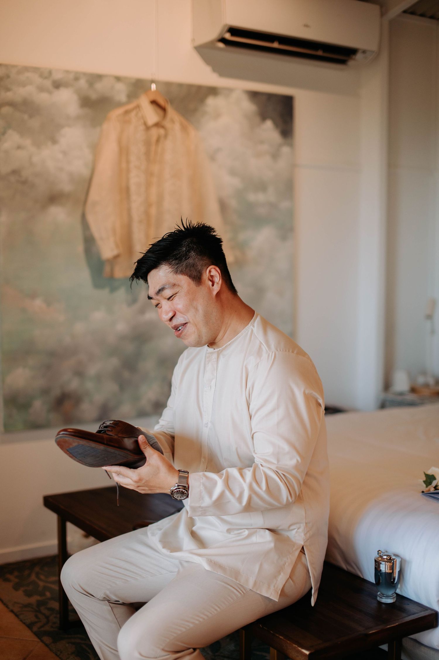 A groom dressed in white examines his footwear while getting ready.