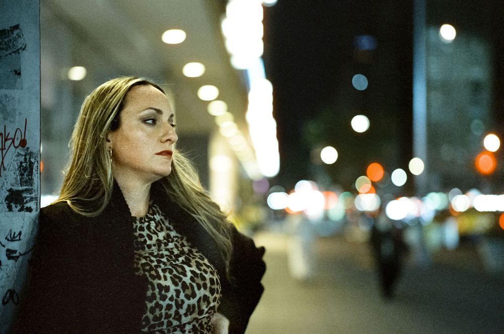 A dramatic nighttime portrait with bokeh city lights and a black coat against an urban backdrop.