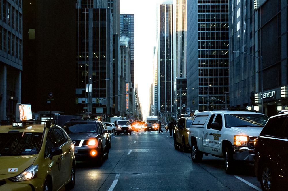 Urban street scene with cars and tall buildings in downtown during evening rush hour.