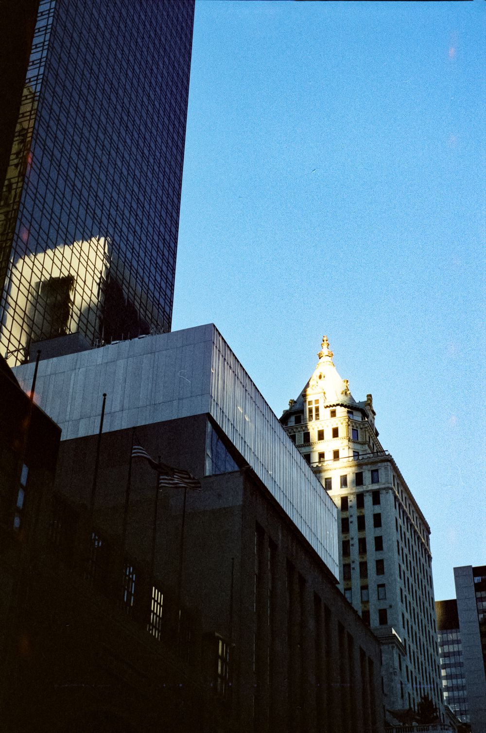 Modern glass skyscraper contrasting with historic architecture against bright blue sky.