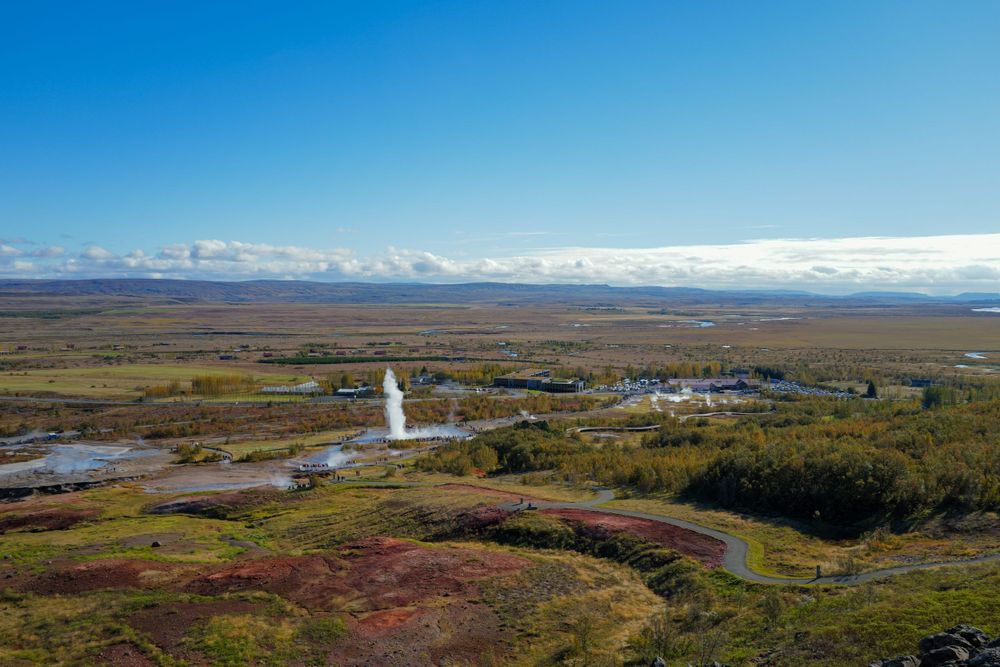 Aerial view of Skalholt church with its white steeple rising from autumn-colored Icelandic landscape and mountains in distance.