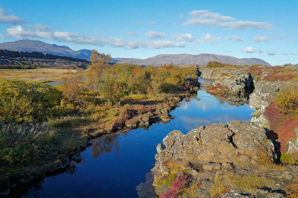Calm river flowing through rocky terrain at Thingvellir National Park in Iceland with mountains in the background.
