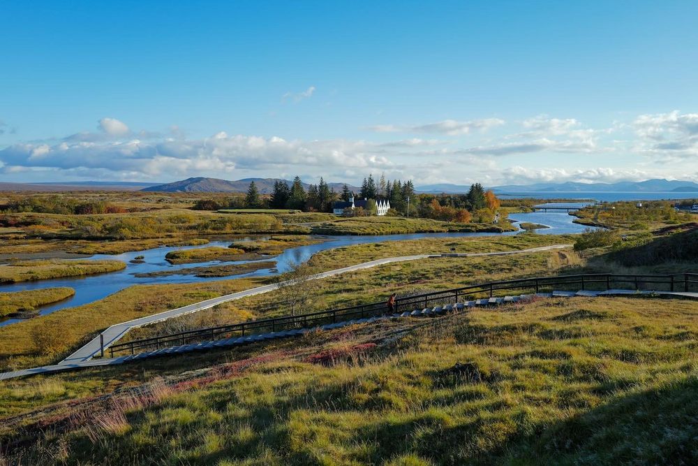 Meandering rivers and wetlands stretch across rugged Icelandic landscape under cloudy blue skies.