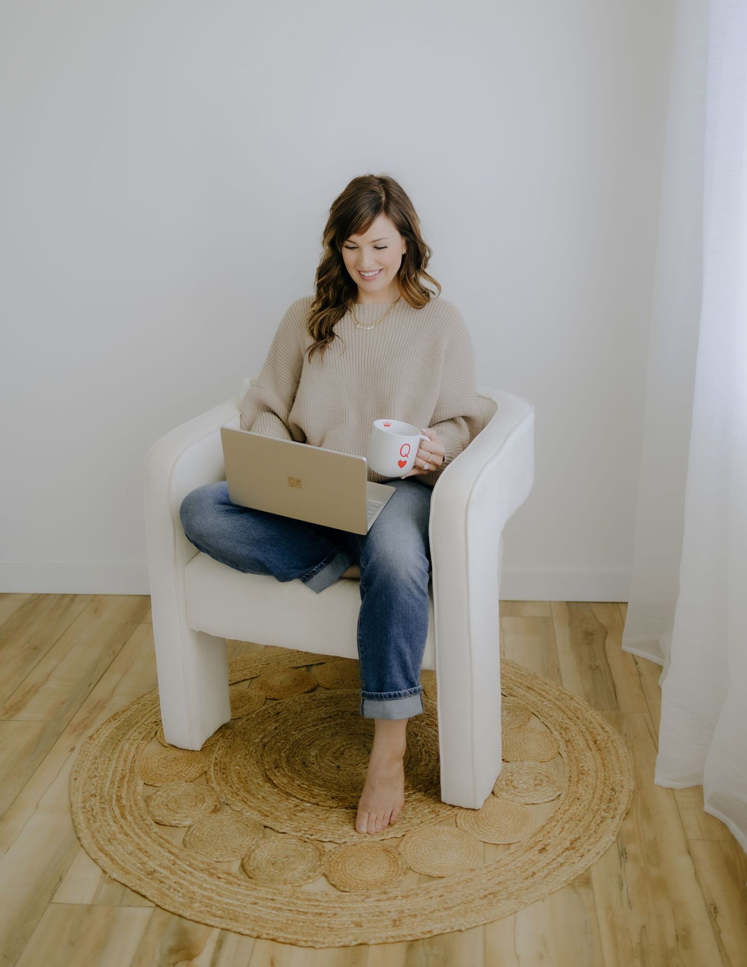 Person relaxing with laptop in cozy white chair on circular rug.