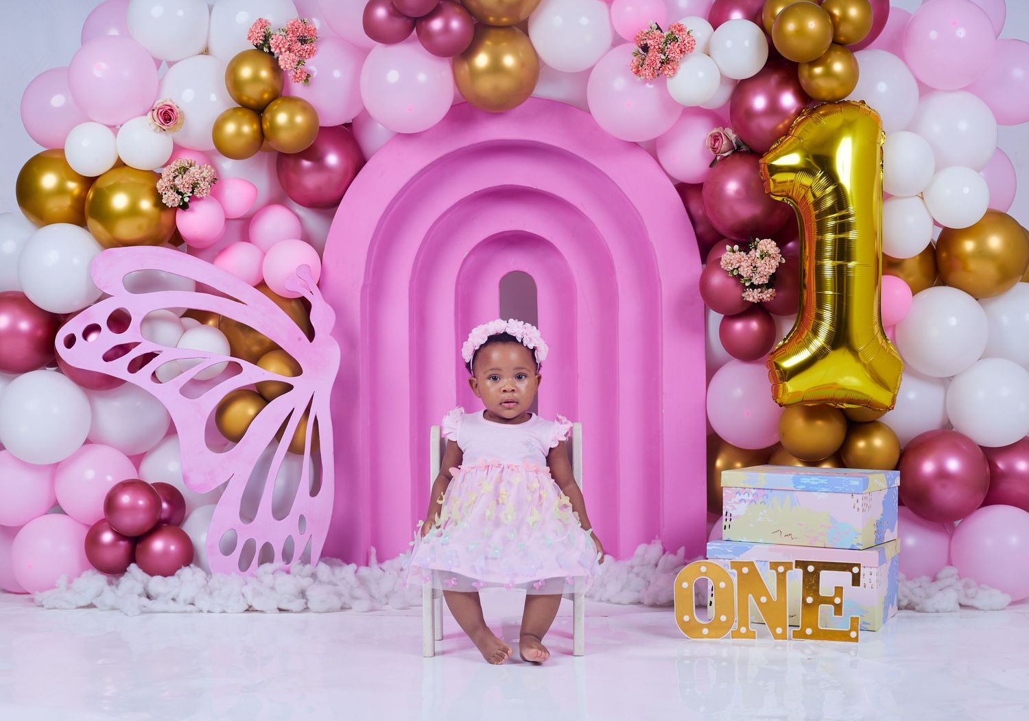 First birthday celebration setup with pink arch, balloons and gold number one decoration.
