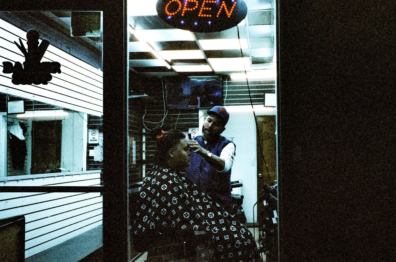 Person working behind counter with neon open sign in window at night.