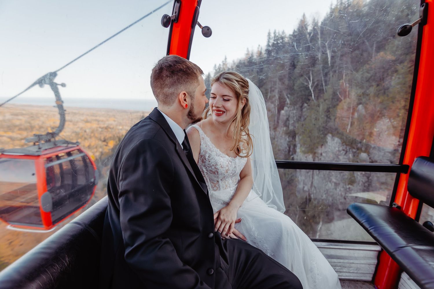 A couple shares an intimate moment while riding in a red gondola lift over a scenic winter landscape.