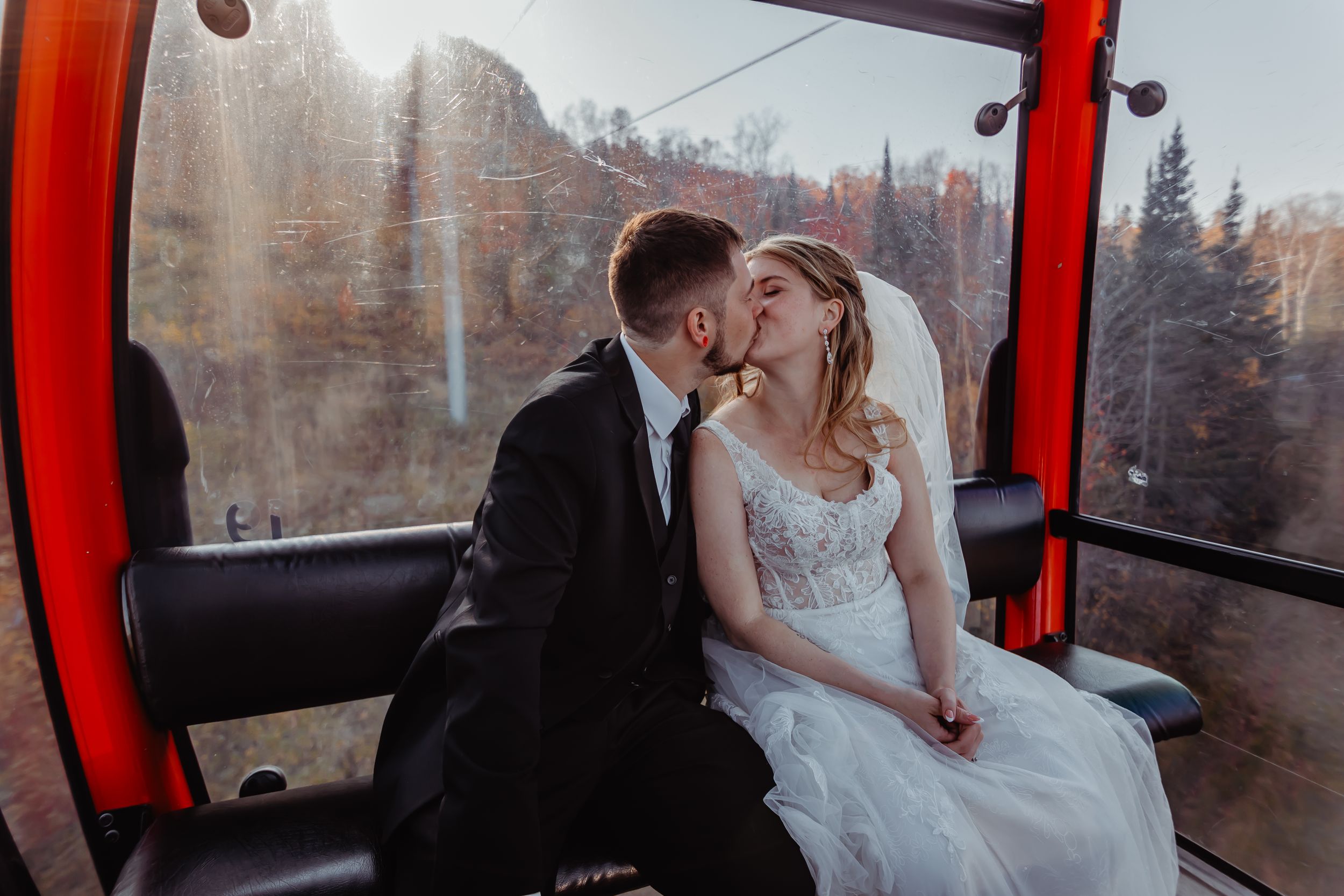 Tender moment shared between newlyweds in red gondola against winter mountain scenery.