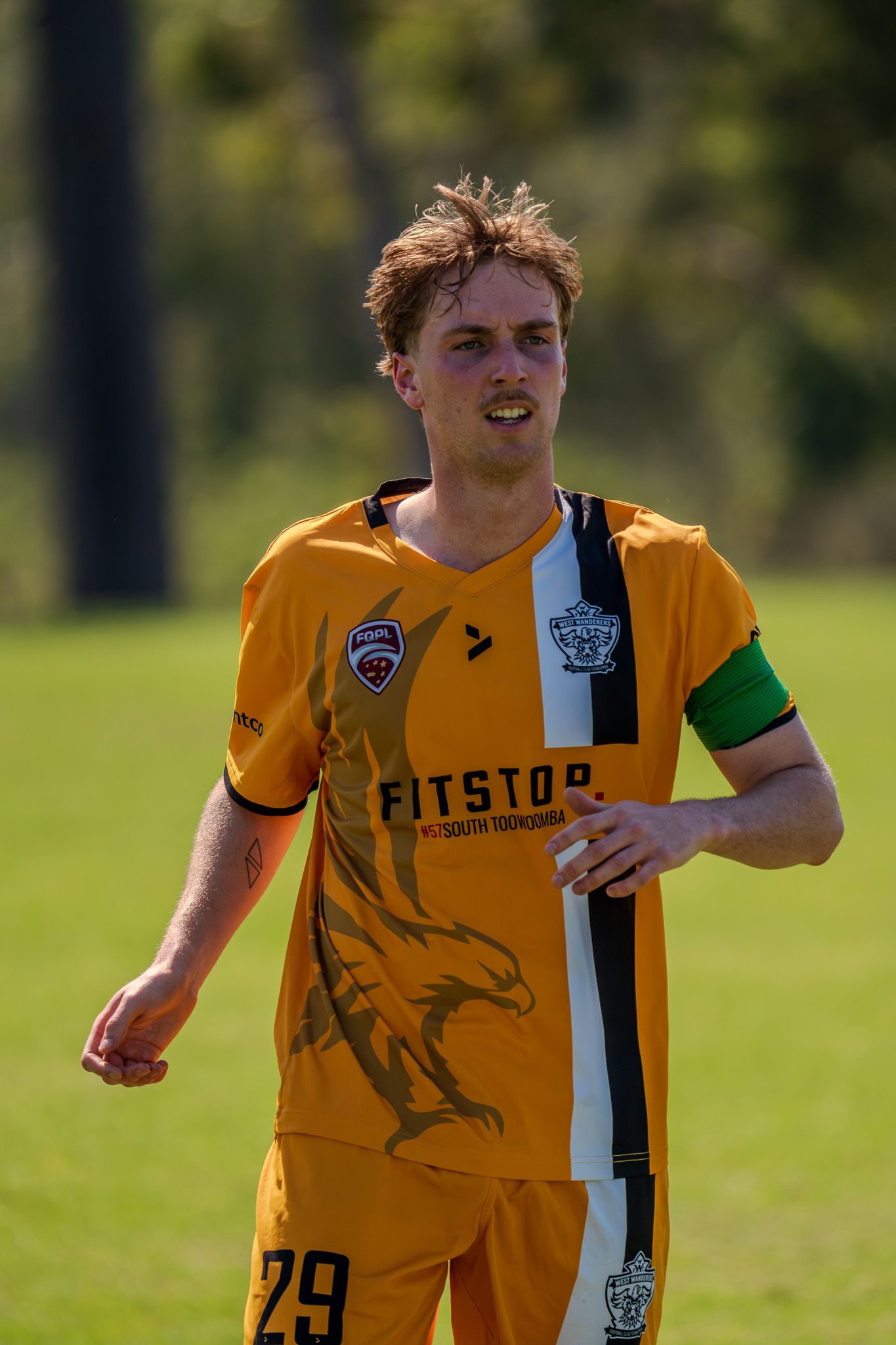Soccer player wearing yellow jersey with number 29 and captain's armband stands on grass field.