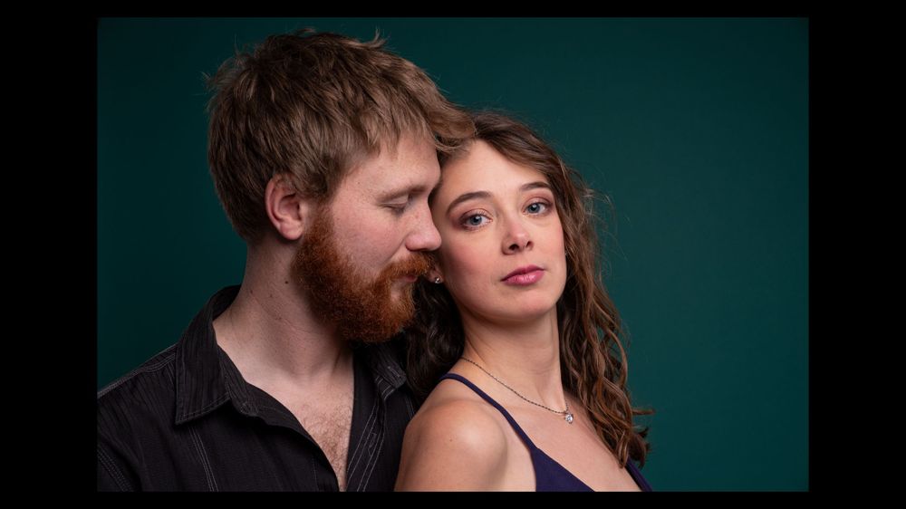 Intimate portrait of a couple against teal background with dramatic lighting.