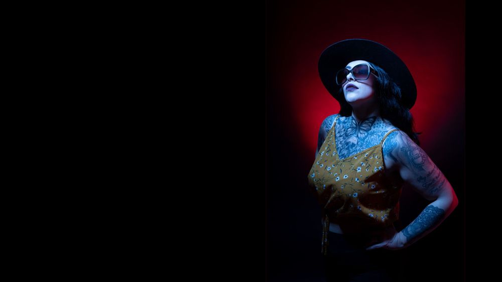 Dramatic portrait with blue lighting of a performer in a hat against a dark red background.
