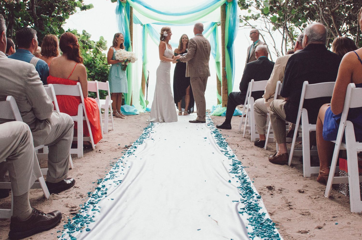 A beach wedding ceremony setup with turquoise decor and white aisle runner lined with blue petals.