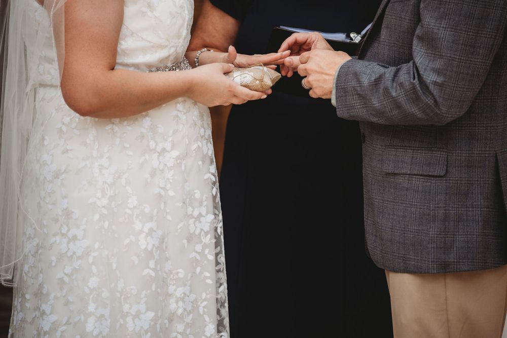 Couple exchanging rings at outdoor ceremony with white floral arch in Lafayette, LA