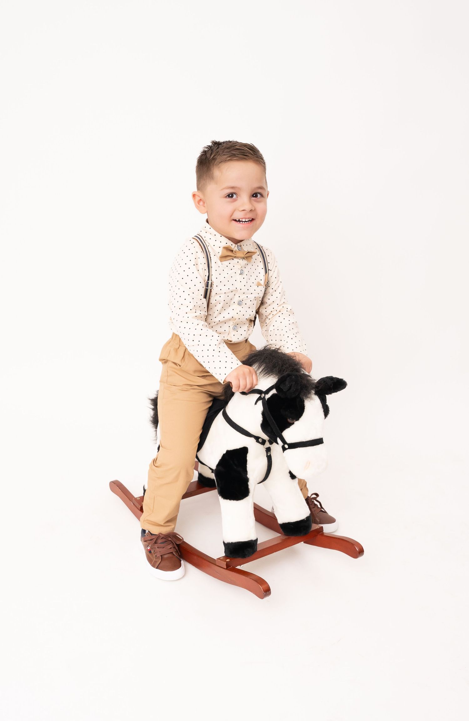 A toddler riding a black and white rocking horse toy against a white background.