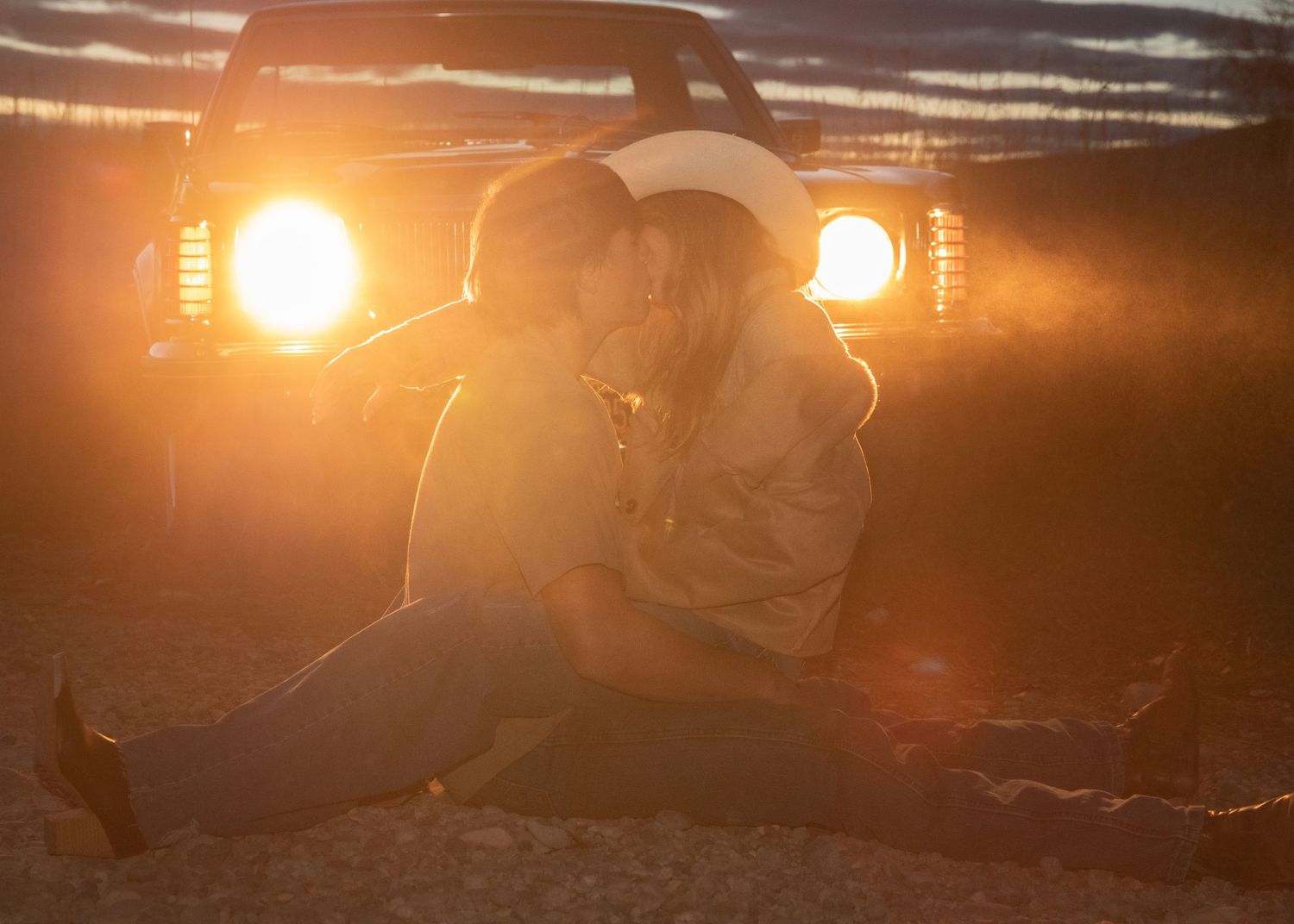 Silhouette against truck headlights at sunset in rustic outdoor setting.