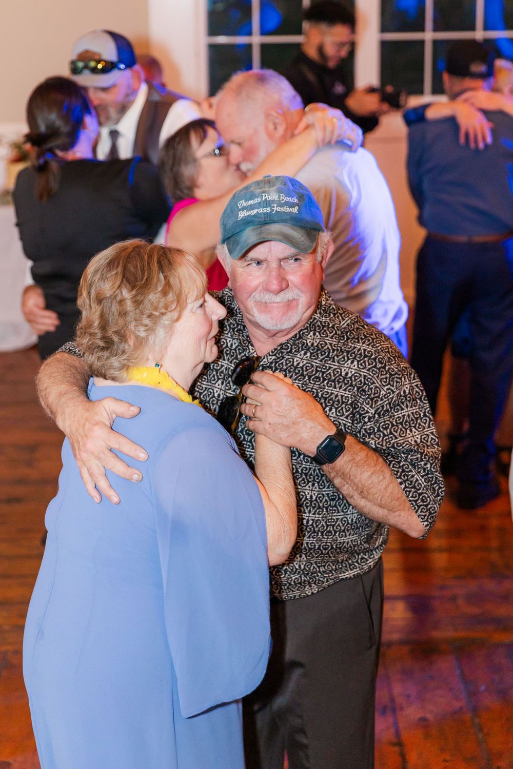 Couples dancing and embracing at a wedding reception on a wooden dance floor.