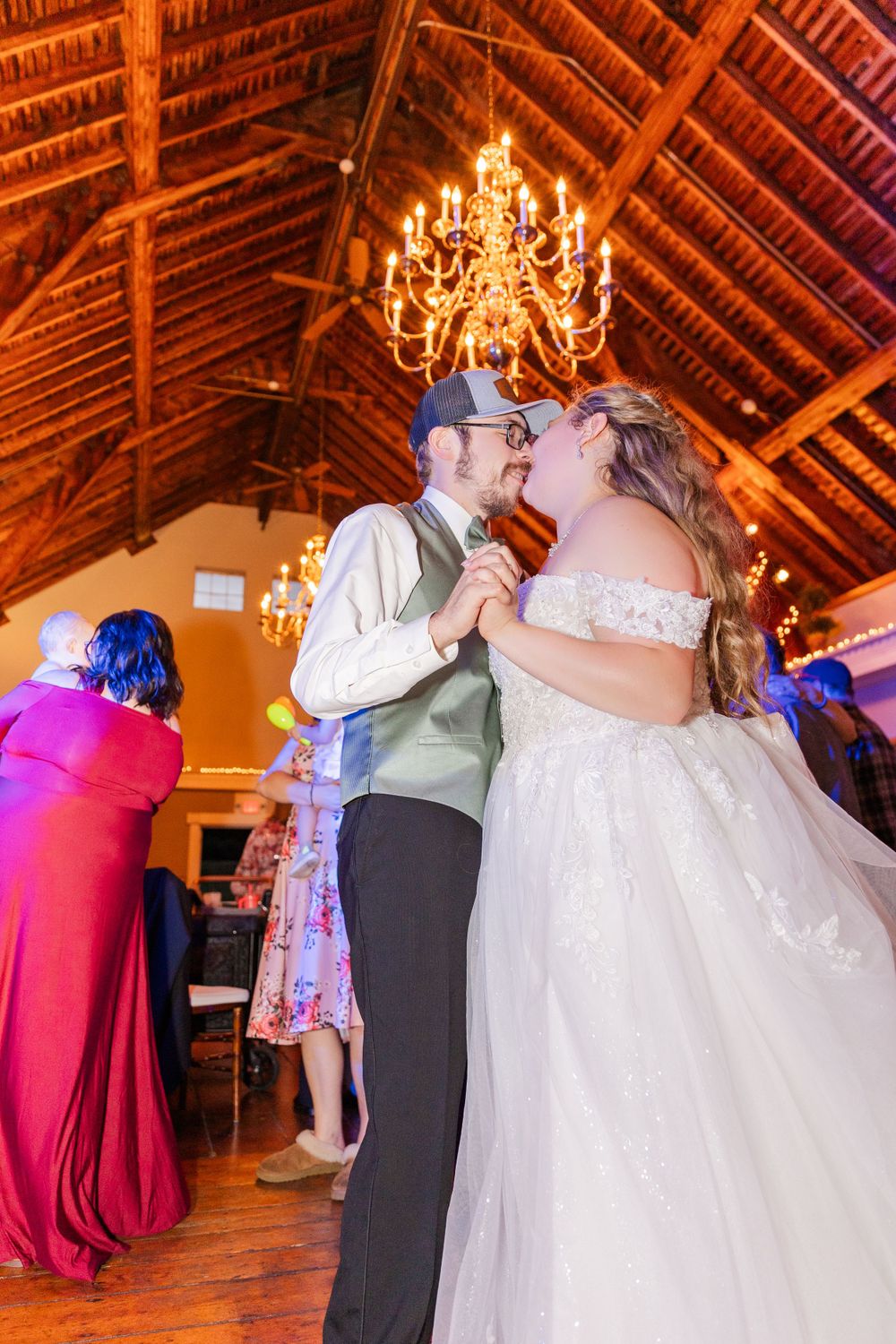 A couple shares a romantic dance under a rustic wooden ceiling with a glowing chandelier.
