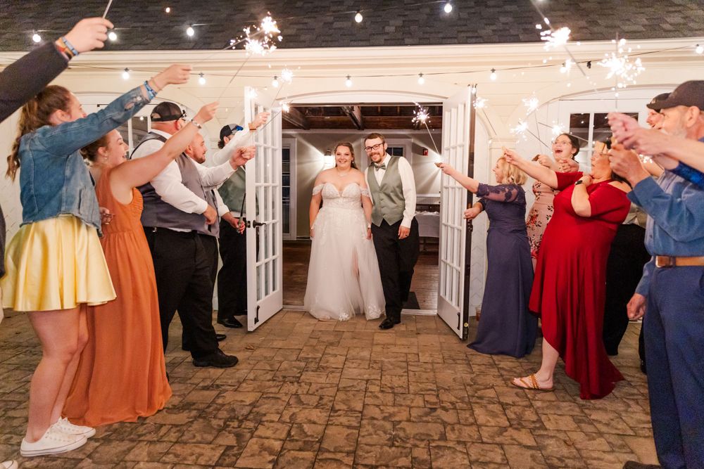 Guests form a sparkler tunnel as newlyweds exit through white french doors on stone patio.