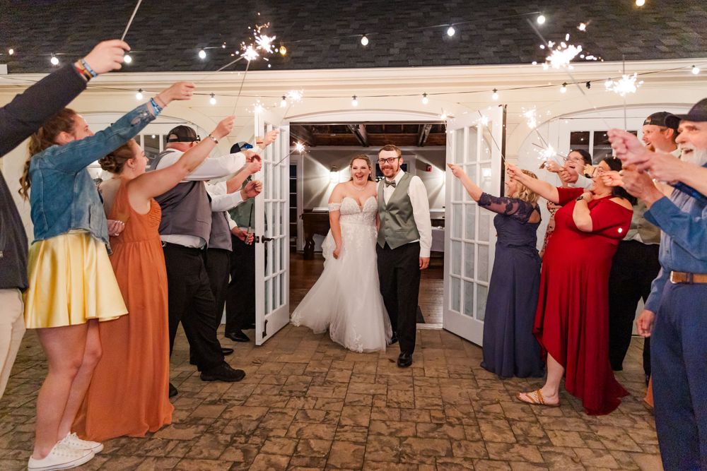 Wedding party creates sparkler exit tunnel for couple on decorative stone patio with french doors.