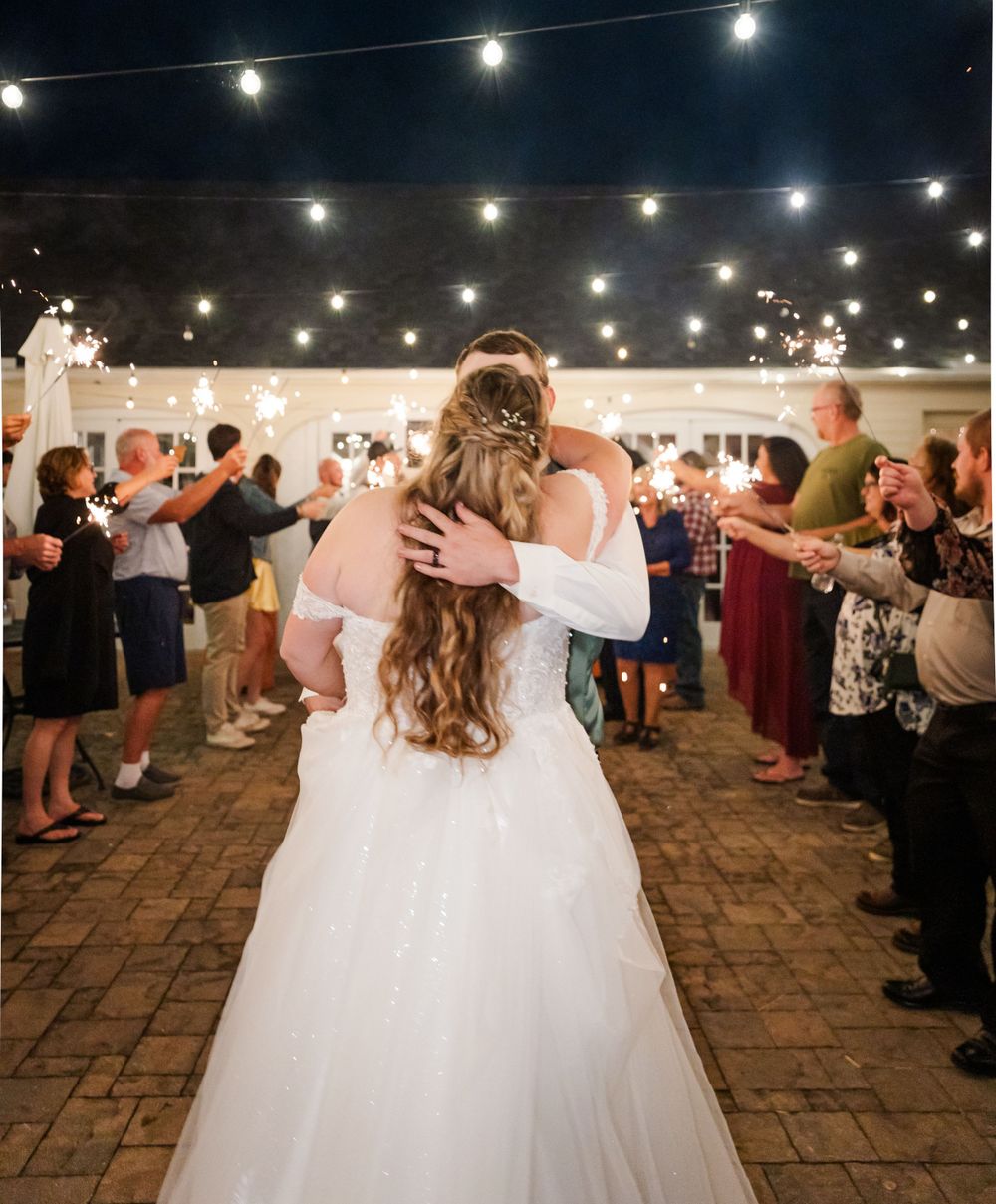 Couple embraces during their sparkler exit celebration with string lights overhead.