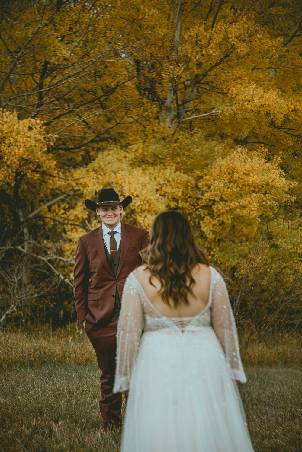 A couple in wedding attire exchanges glances in front of vibrant yellow fall foliage on their autumn wedding day.