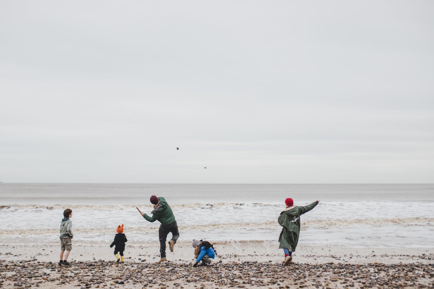 Group playing and throwing rocks on rocky beach under overcast sky.