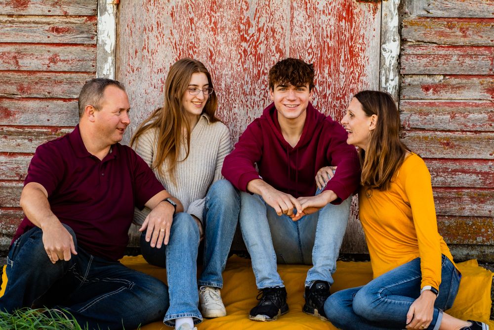 Casual group sitting together against weathered red barn wall background.