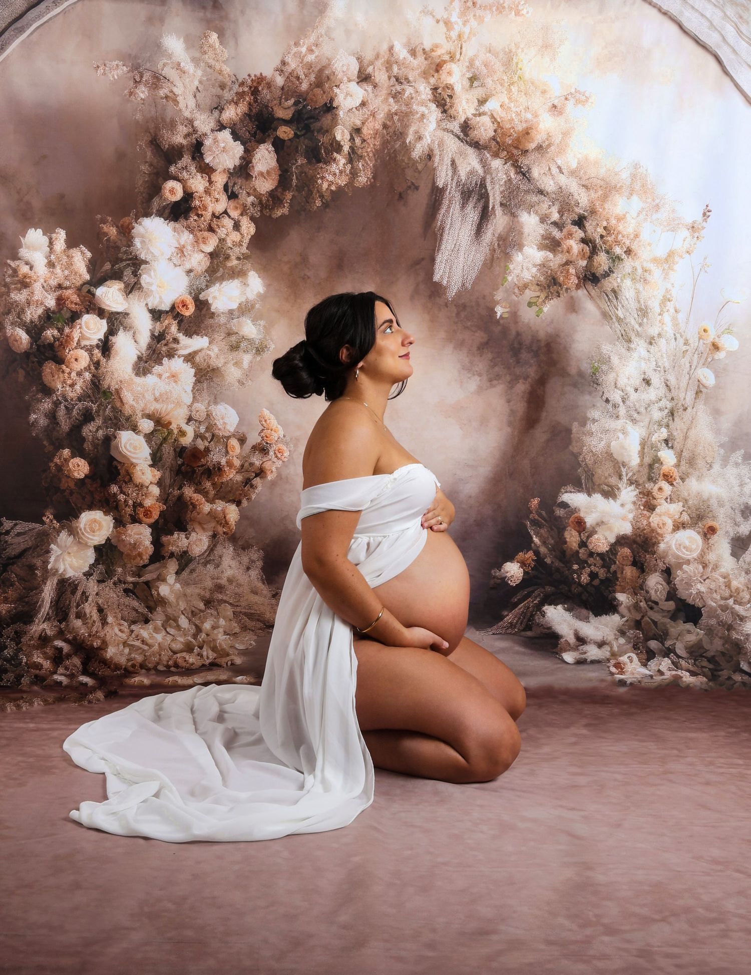 Artistic maternity portraits with flowing white fabric against ethereal floral wall.