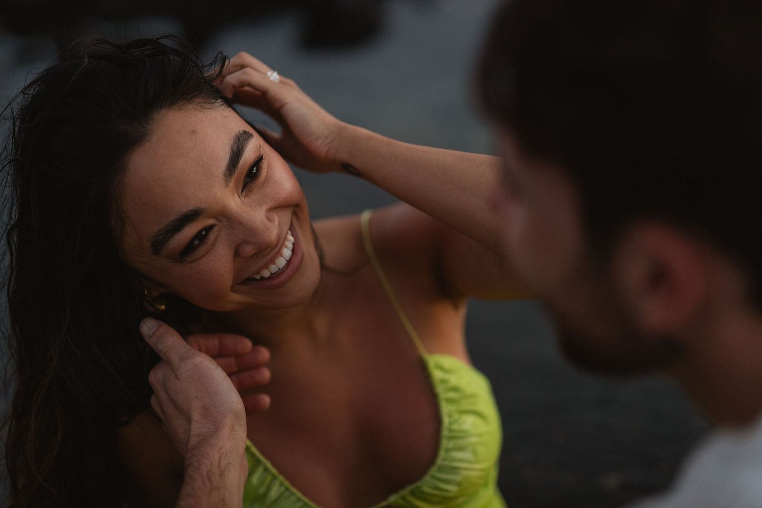 Woman in yellow dress smiling warmly as man gently touches her face during intimate couples portrait session.