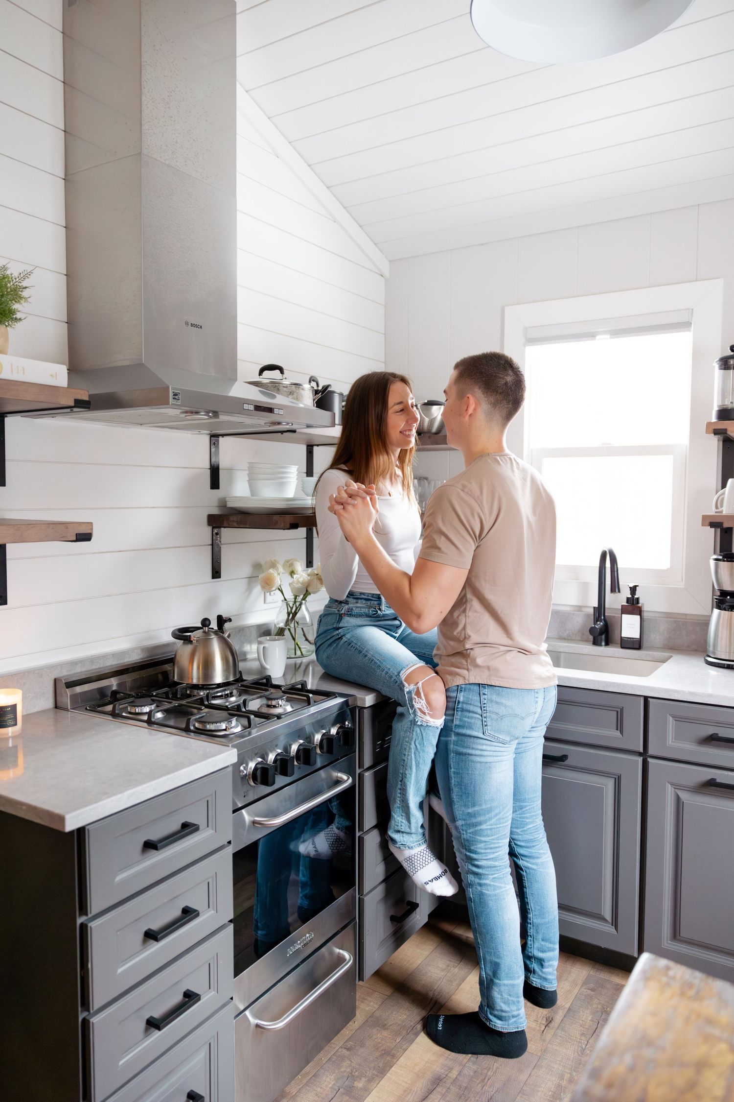 Modern grey and white kitchen interior with couple sharing intimate moment by stove.