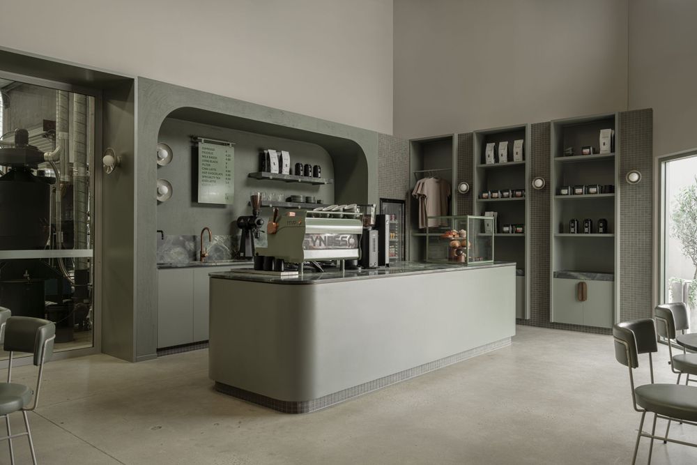 Modern minimalist cafe interior with espresso machine and shelving displays in muted gray and white tones.