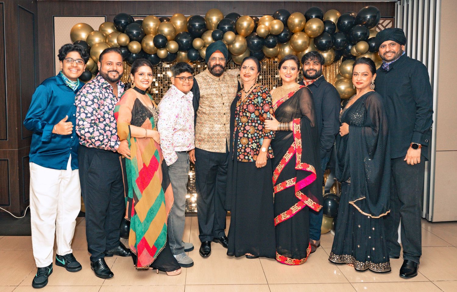 Celebration group photo with people in formal attire against black and gold balloon backdrop.