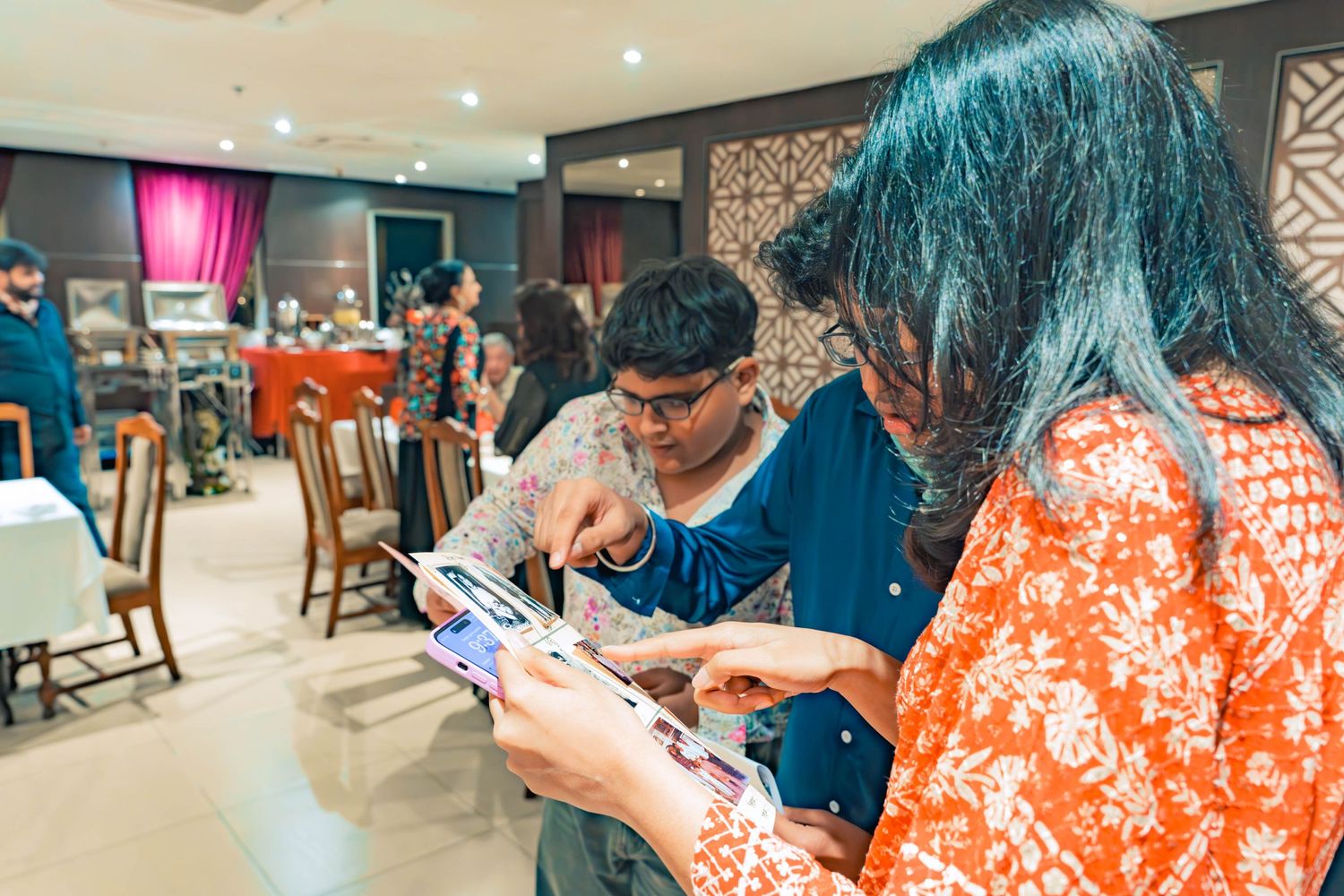 People looking down at papers during an indoor event with decorative wall patterns visible.