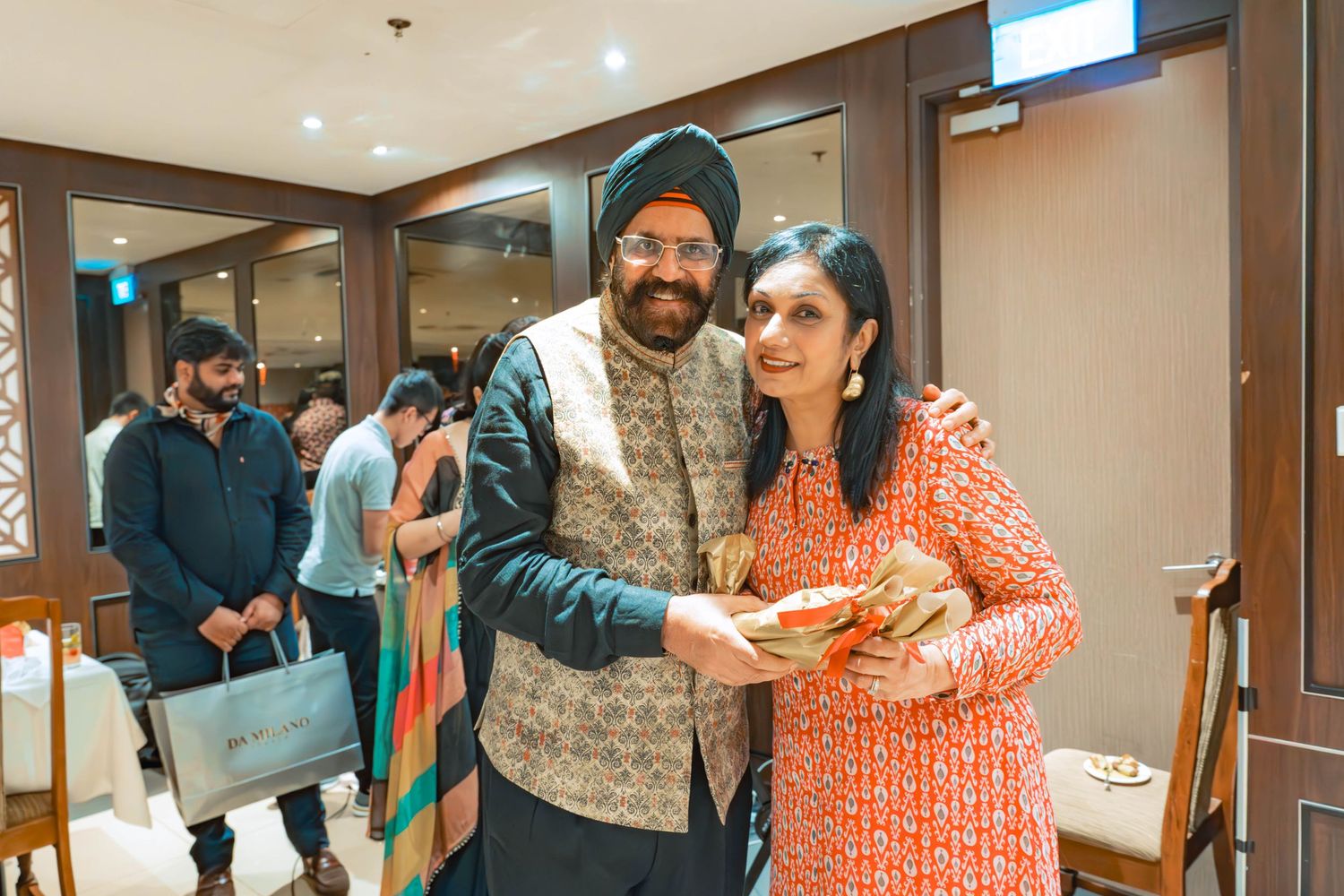 Guests mingle and socialize at an indoor cultural celebration with traditional Indian attire.