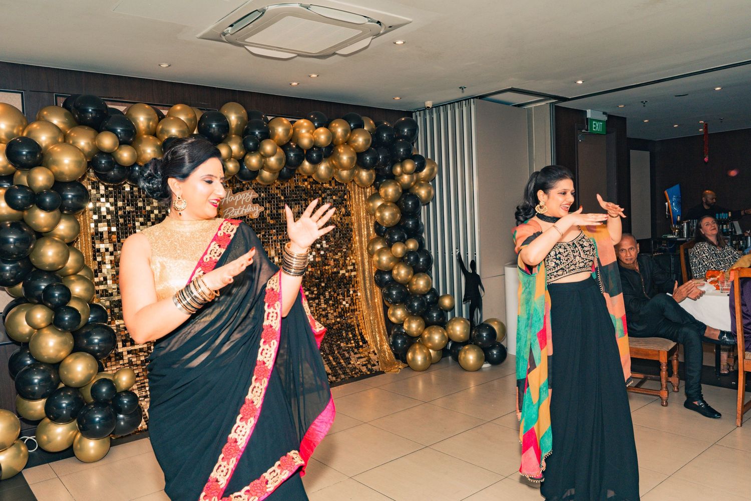 People dancing and celebrating at a party with gold balloon decorations in the background.